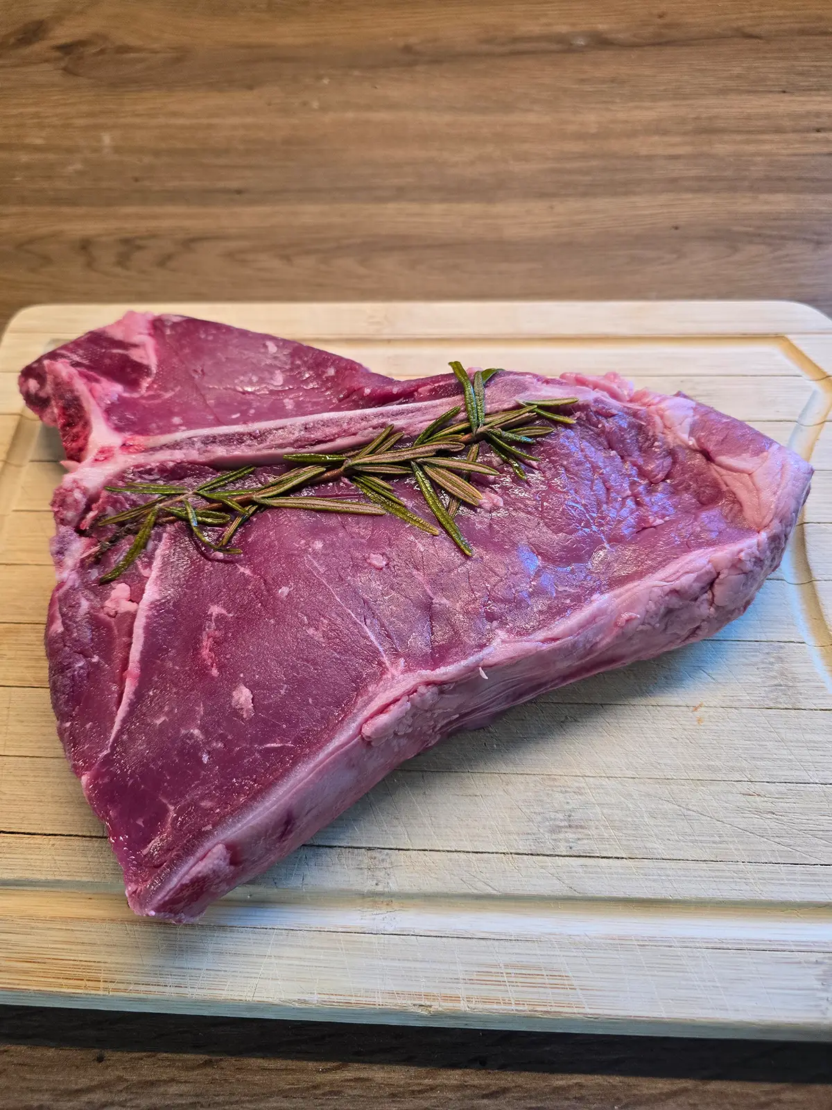 Chianina-Rind: Herkunft, Fleisch, IGP und richtige Zubereitung Rohes Chianina-Steak auf dem Holzbrett mit Rosmarin